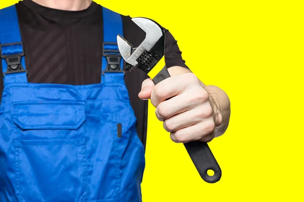 Mechaniker in Arbeitskleidung hält einen Schraubenschlüssel in der Hand, isoliert auf gelbem Hintergrund — Stockfoto