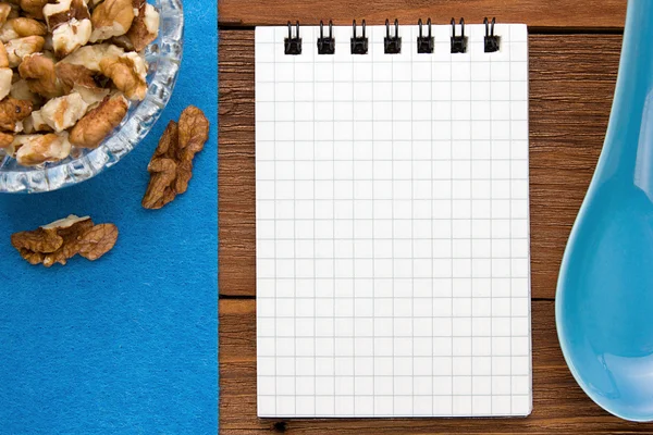 Menu background. Cook book. Recipe notebook with walnuts on a blue background and a wooden board.