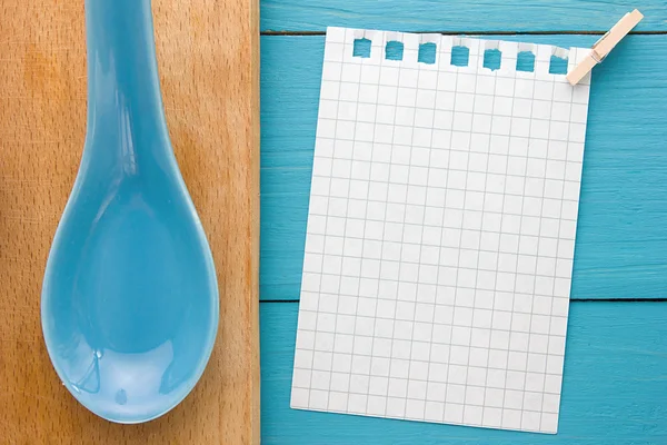 For recording cooking recipes and kitchens. A piece of paper with a pin on turquoise yellow-blue wooden Board and clay spoon — Stock Photo, Image