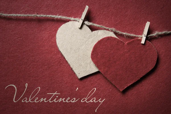 Alla hjärtans dag. Två hjärtan från filt och kartong på rep med klädnypa på röd bakgrund lutning — Stockfoto