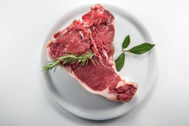 Çiğ biftek, defne yaprağı ve beyaz yuvarlak tabakta biberiye.