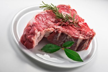 Çiğ biftek, defne yaprağı ve beyaz yuvarlak tabakta biberiye.