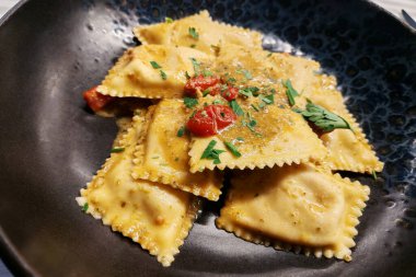 Domatesli ve maydanozlu, yuvarlak siyah bir tabakta balık mantısı.