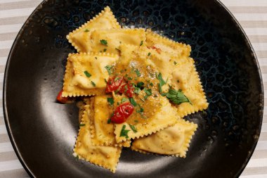 Domatesli ve maydanozlu, yuvarlak, siyah bir tabakta balık mantısı.