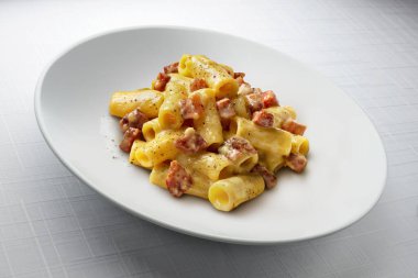 Beyaz arka planda izole edilmiş beyaz bir tabakta Rigatoni Carbonara Makarnası