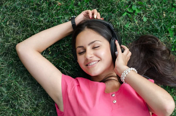 Pretty teenage girl lying on the grass listening to music — Stock Photo, Image