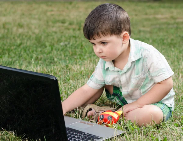 Niño pequeño con un portátil me siento en el prado —  Fotos de Stock