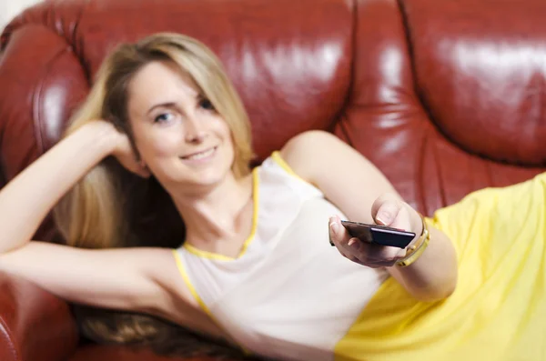 Chica en un sofá de cuero con control remoto — Foto de Stock