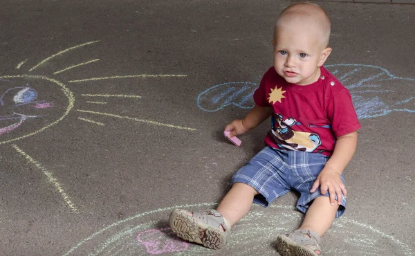 Kleine jongen trekt met krijt op de stoep zon — Stockfoto