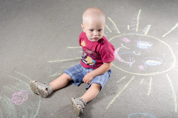 Kleine jongen trekt met krijt op de stoep zon — Stockfoto