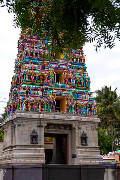 Небоскреб крупным планом со всеми деталями архитектуры. Многоцветная башня храма на юге Индии в окружении деревьев