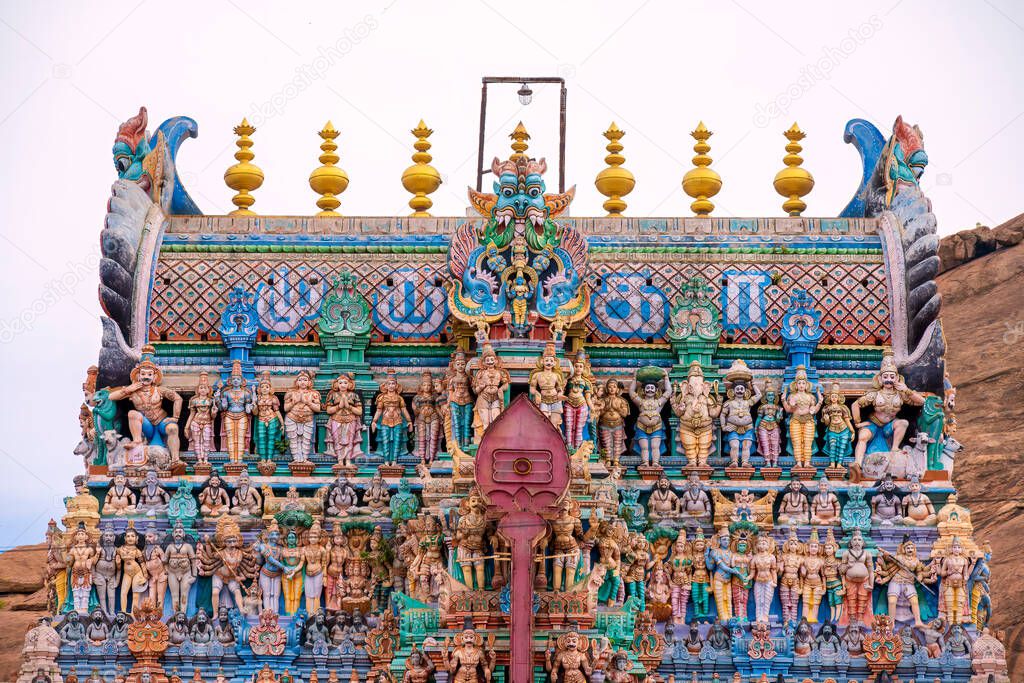 Old south indian temple in close up with full architecture details. Multi colour temple tower in south India surrounded by mountains and rock
