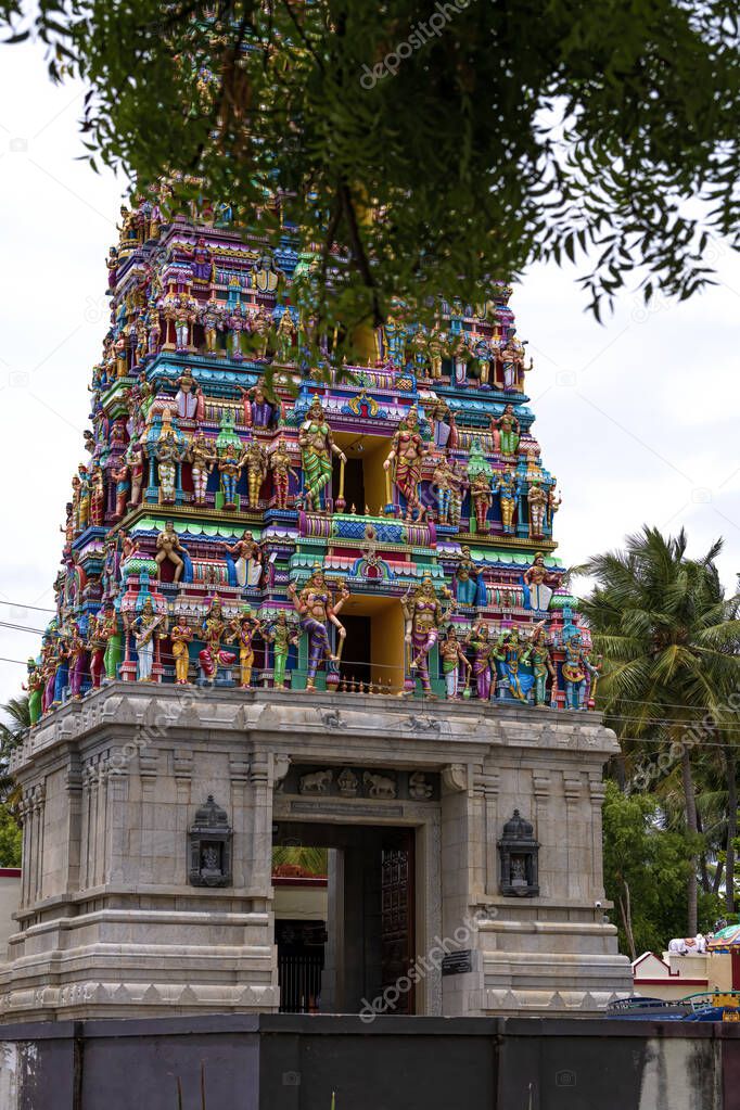 Temple tower in close up with full architecture details. Multi colour temple tower in south India surrounded by the trees