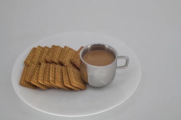 Indian tea on a sliver cup and Wheat biscuits in the white plate with white background. Indian biscuits popularly known as Chai-biscuit in Indi