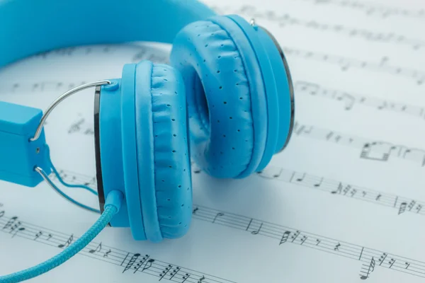 Niebieski słuchawki na tło Uwaga muzyki arkuszy. — Zdjęcie stockowe