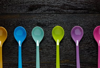 Ahşap masa arka plan üzerinde renkli plastik kaşıkla Üstten Görünüm.