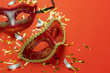 Masa üstü görüntü güzel renkli karnaval festivali arka planı. Düz nesne ev ofis masası stüdyosundaki modern kırmızı kağıdın üzerinde süslü maske ve dekor konfetileri uzanıyordu. Kopya alanı.