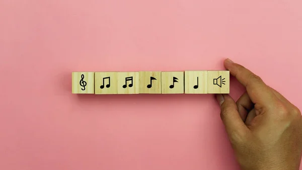 Music and  art entertainment instruments background concept.Close up Asian young man holding musical note icon on cube blocks wooden.Objects stack arrangement on pink paper background.copy space.