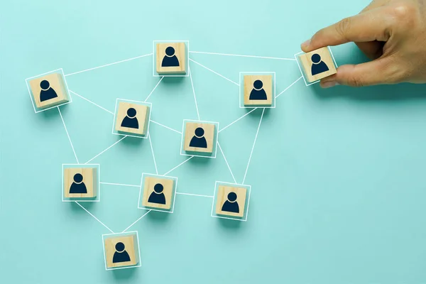 Top view of human resources and recruiting business or team leader concepts. Hand adult Asian man holding of people icon community on wooden cube block. Objects on blue paper background. copy space .