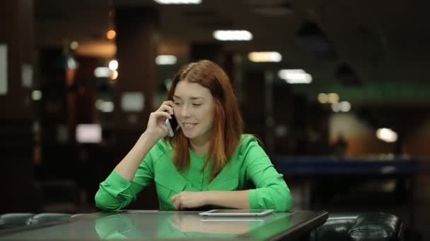 Krásná žena sedí u stolu v kavárně a mluví na mobilu bílé barvy.