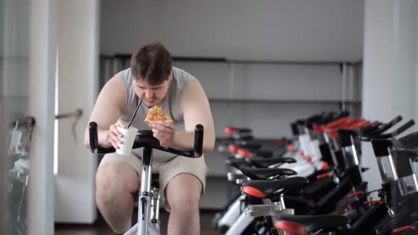 Thick guy practices on an exercise bike, stopping to eat pizza and  continues to train — Stock Video © work_for_stock #109403562