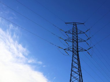 Yüksek voltajlı pilon ve beyaz bulutlu mavi bir gökyüzü. Aktarım kulesi uzun mesafelerde elektrik taşımak için kullanılır..