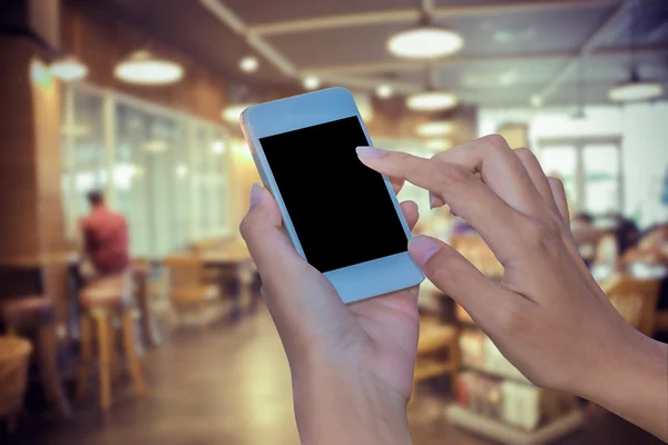 Woman hand holding smartphone on apstract blured coffee shop background soft focus