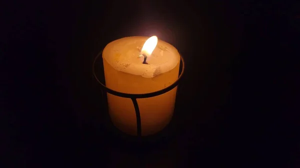 Burning candle, yellow wax candle in black candleholder on black background, isolated candle. Flame, fire, candlelight.