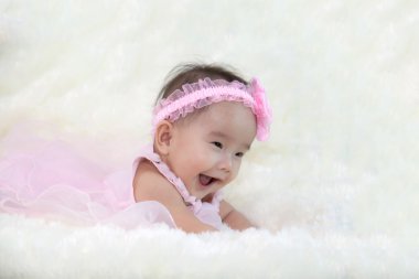 Şirin beş ay Asya bebek ile pembe elbise., parlak yumuşak halı üzerinde gülüyor.