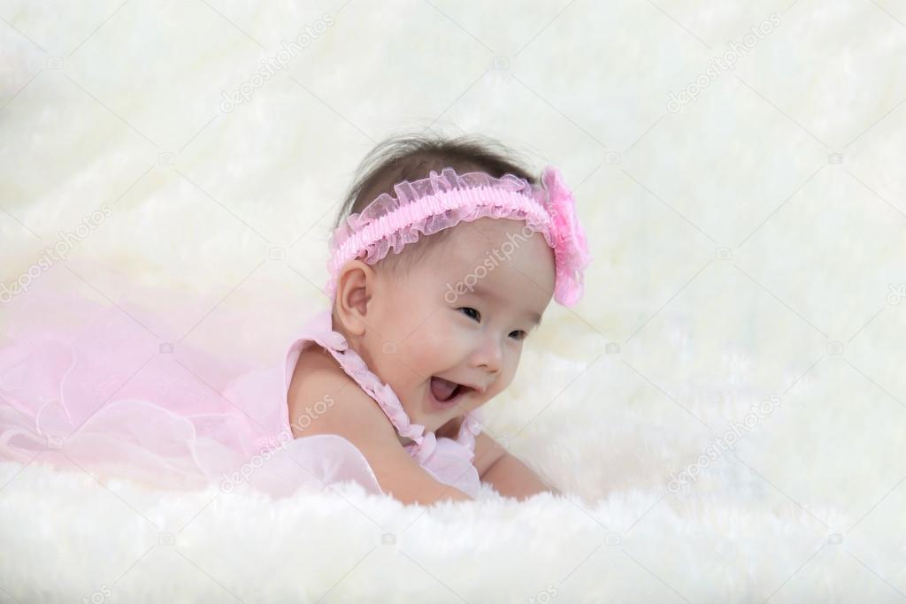 Cute five months asian baby laughing with pink dress., on bright soft carpet.