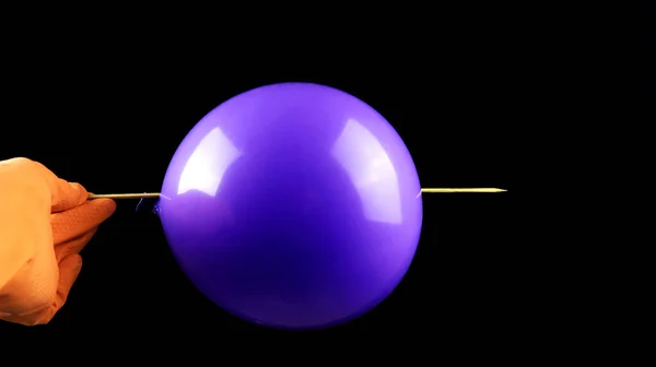 Bir el, bir balonu patlamadan şişle delme eylemini gösteriyor. Bilim konsepti balon kullanıyor.