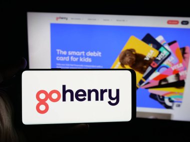 Stuttgart, Almanya - 10-08-2025: Fintech şirketi GoHenry Limited 'in logosuna sahip akıllı telefon sahibi kişi web sitesinin önünde ekranda. Telefon ekranına odaklan.