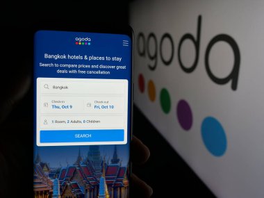 Stuttgart, Almanya - 10-09-2025: İnternet seyahat şirketi Agoda Company Pte 'nin internet sayfası ile cep telefonu tutan kişi. Logonun önündeki Ltd ekranda. Telefon ekranının merkezine odaklan.