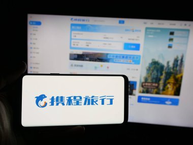 Stuttgart, Almanya - 10-09-2025: İnternet sitesinin önünde ekranda Çinli seyahat şirketi Ctrip 'in logosunun bulunduğu akıllı telefonu tutan kişi. Telefon ekranına odaklan.
