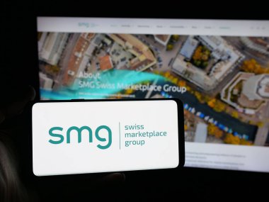 Stuttgart, Almanya - 10-09-2025: SMG İsviçre Piyasa Grubu AG logosuna sahip akıllı telefon sahibi kişi web sitesinin önünde ekranda. Telefon ekranına odaklan.