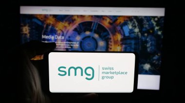 Stuttgart, Almanya - 10-09-2025: SMG İsviçre Pazaryeri Grubu AG logosuna sahip cep telefonu sahibi kişi web sayfası önünde ekranda. Telefon ekranına odaklan.