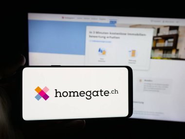 Stuttgart, Almanya - 10-09-2025: Üzerinde İsviçreli emlak portalı şirketi Homegate 'in logosu olan akıllı telefonu web sitesinin önünde tutan kişi. Telefon ekranına odaklan.