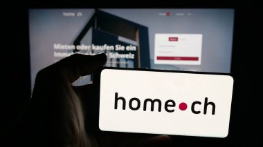 Stuttgart, Almanya - 10-09-2025: Üzerinde İsviçreli emlak portalı şirketi Home.ch 'in logosu olan cep telefonu bulunan kişi web sitesinin önünde ekranda. Telefon ekranına odaklan.