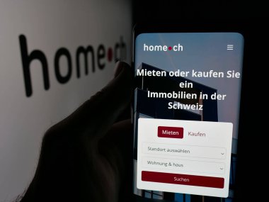 Stuttgart, Almanya - 10-09-2025: İsviçreli emlak portalı şirketi Home.ch 'in web sayfası ile akıllı telefonu olan kişi logonun önünde ekranda. Telefon ekranının merkezine odaklan.
