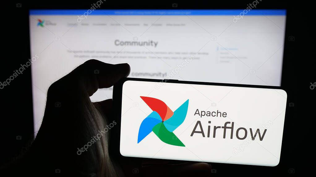 Stuttgart, Germany - 10-08-2025: Person holding mobile phone with logo of workflow management platform Apache Airflow on screen in front of web page. Focus on phone display.