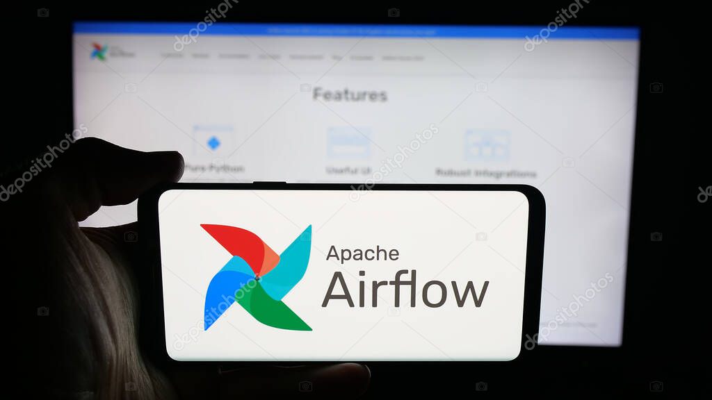 Stuttgart, Germany - 10-08-2025: Person holding cellphone with logo of workflow management platform Apache Airflow on screen in front of webpage. Focus on phone display.