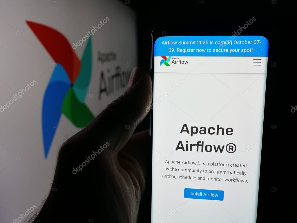 Stuttgart, Germany - 10-08-2025: Person holding smartphone with web page of workflow management platform Apache Airflow on screen in front of logo. Focus on center of phone display.