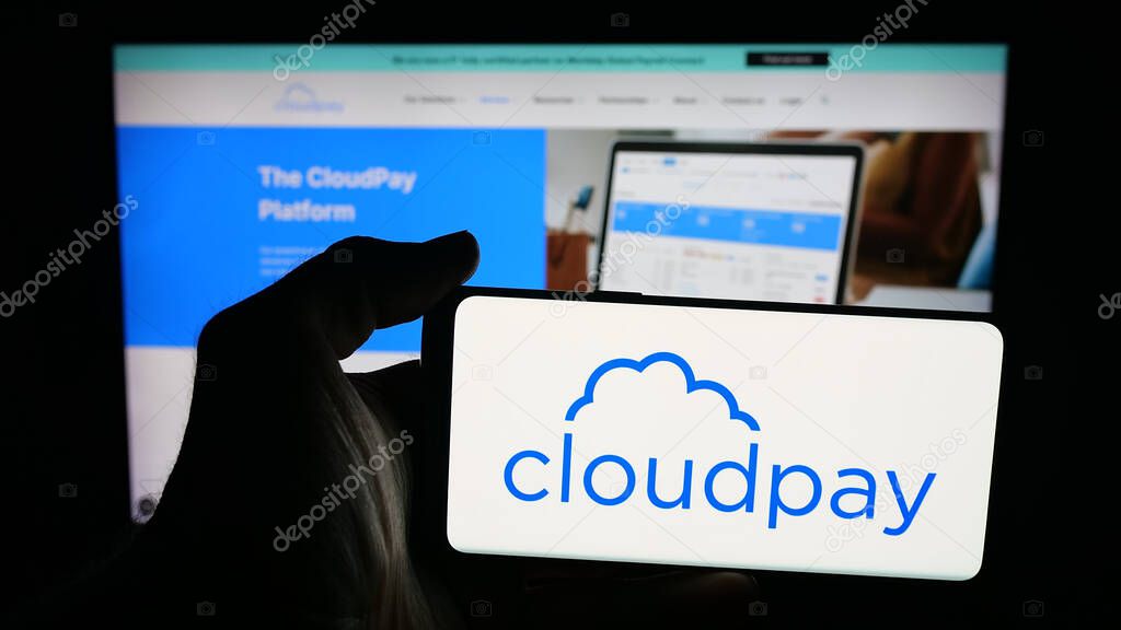 Stuttgart, Germany - 10-08-2025: Person holding mobile phone with logo of British payroll services company CloudPay Inc on screen in front of web page. Focus on phone display.