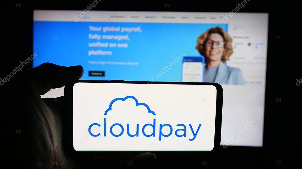 Stuttgart, Germany - 10-08-2025: Person holding cellphone with logo of British payroll services company CloudPay Inc on screen in front of webpage. Focus on phone display.