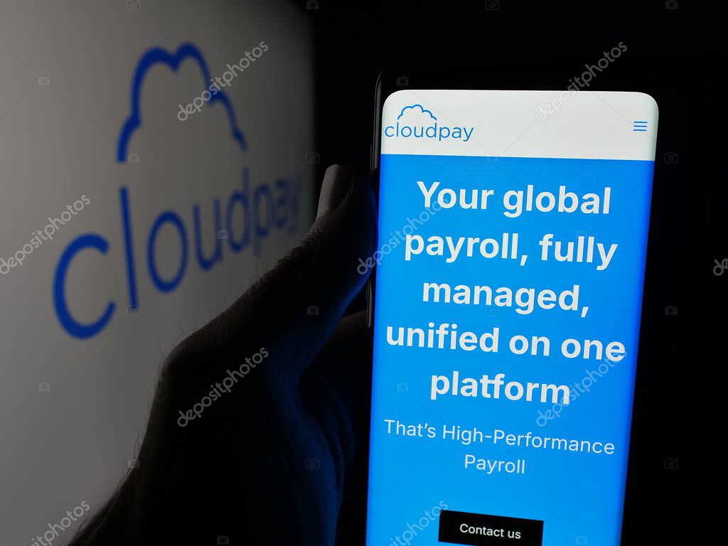 Stuttgart, Germany - 10-08-2025: Person holding smartphone with web page of British payroll services company CloudPay Inc on screen in front of logo. Focus on center of phone display.