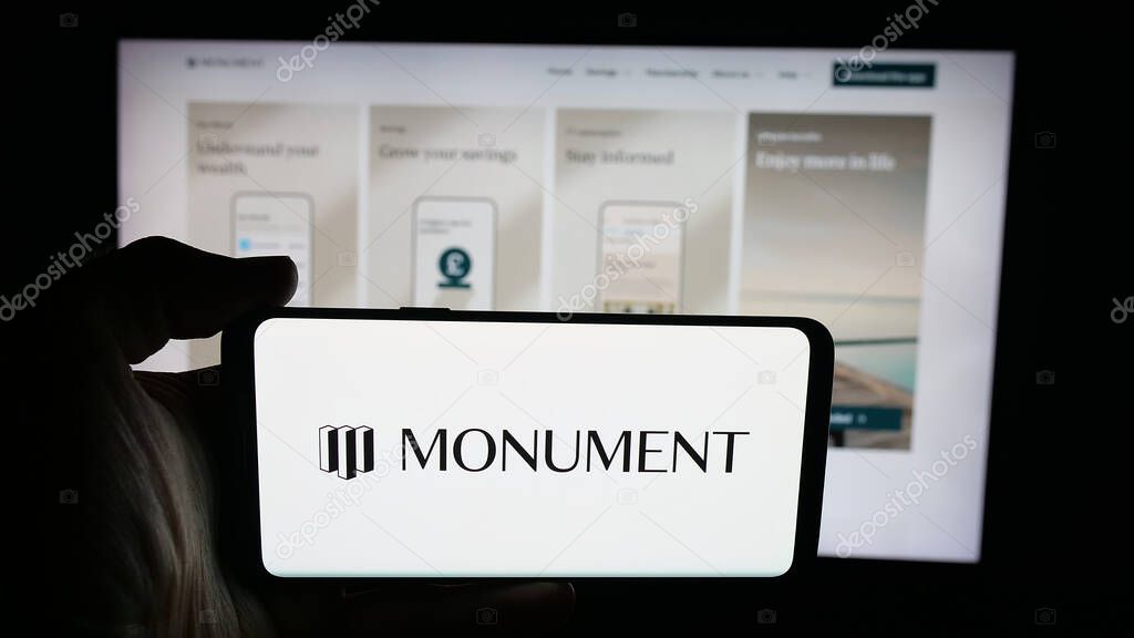 Stuttgart, Germany - 10-08-2025: Person holding cellphone with logo of British banking company Monument Bank Limited on screen in front of webpage. Focus on phone display.