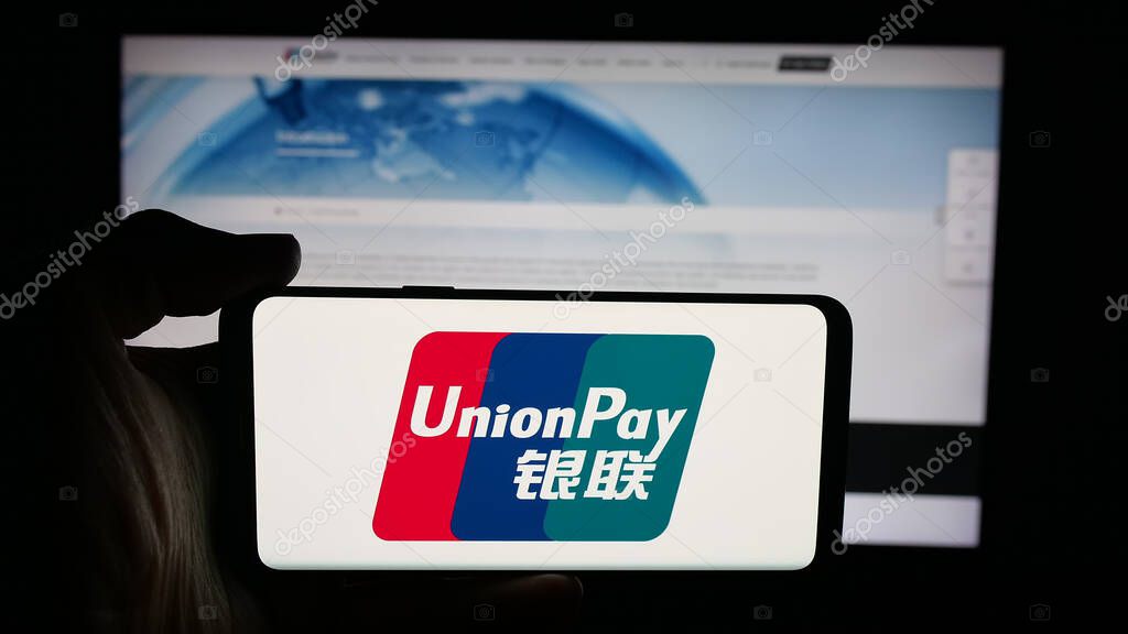 Stuttgart, Germany - 10-08-2025: Person holding cellphone with logo of Chinese credit card company China UnionPay on screen in front of webpage. Focus on phone display.