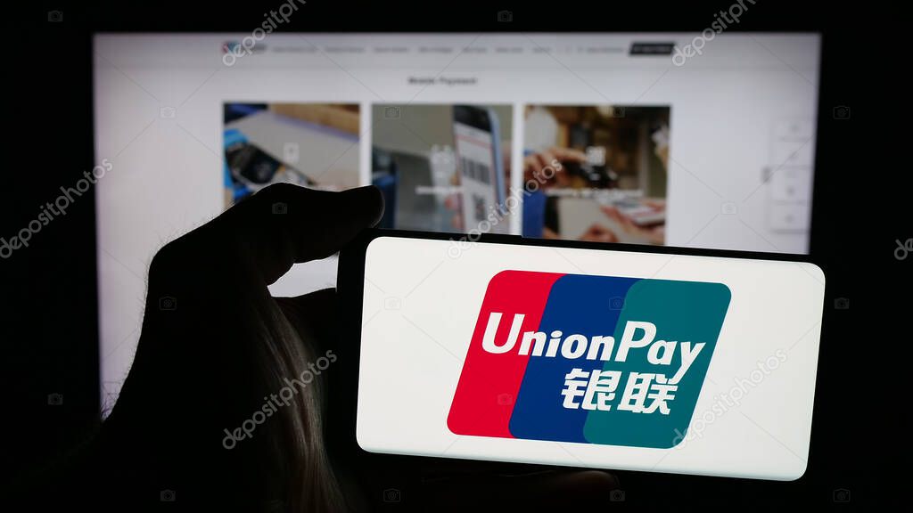 Stuttgart, Germany - 10-08-2025: Person holding mobile phone with logo of Chinese credit card company China UnionPay on screen in front of web page. Focus on phone display.