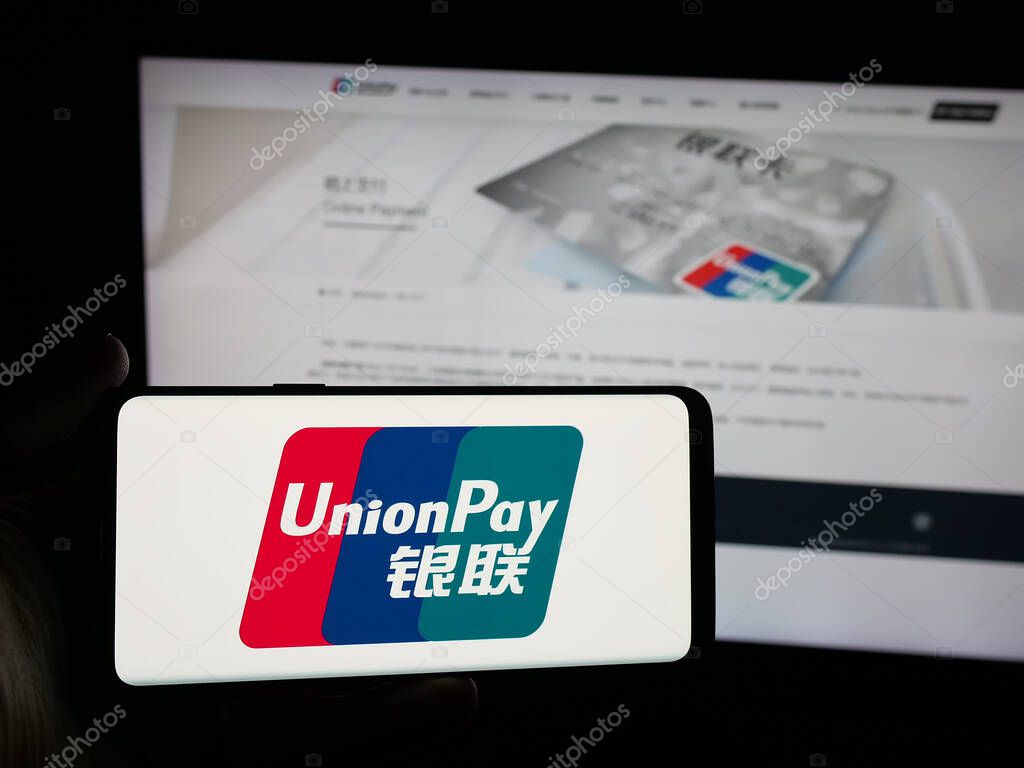 Stuttgart, Germany - 10-08-2025: Person holding smartphone with logo of Chinese credit card company China UnionPay on screen in front of website. Focus on phone display.