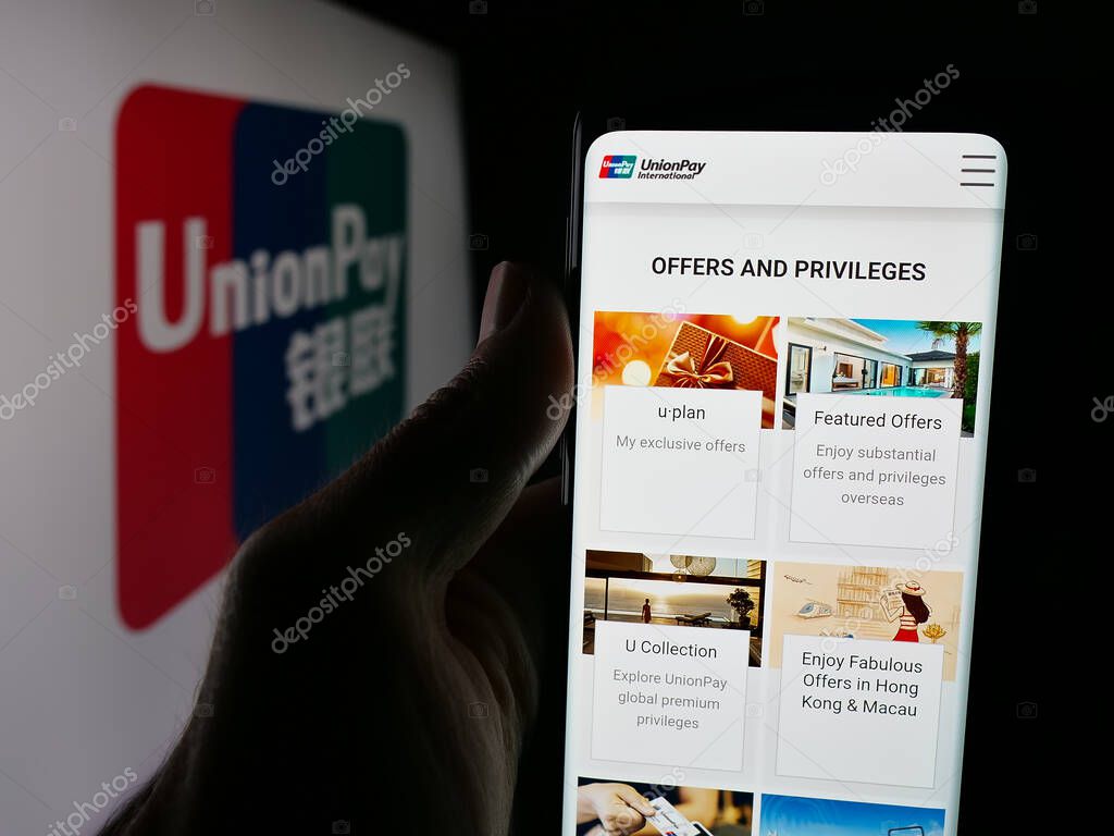 Stuttgart, Germany - 10-08-2025: Person holding smartphone with web page of Chinese credit card company China UnionPay on screen in front of logo. Focus on center of phone display.